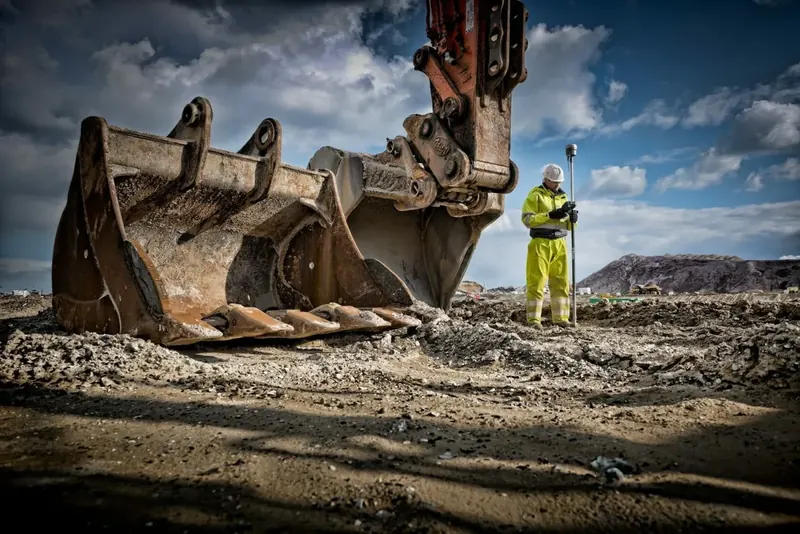 Excavator bucket on a groundworks site with an operative in the background