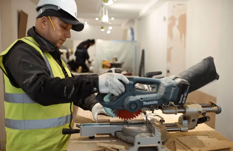 Operative in hi-vis and hard hat cutting timber on a mitre saw during a fit-out