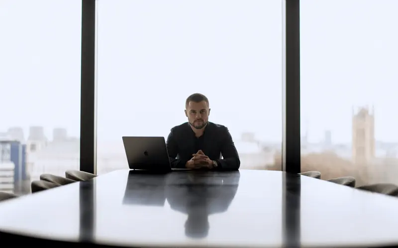 Business owner at a boardroom table with a laptop, city skyline behind