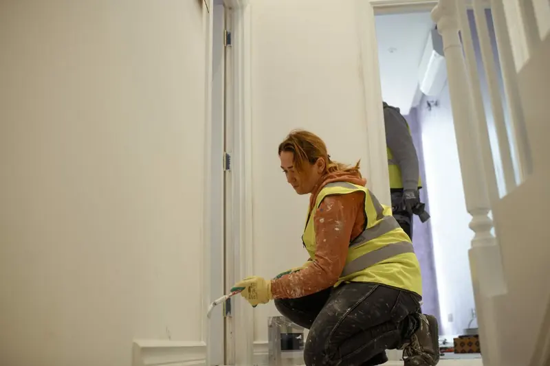 Decorator in hi-vis painting skirting in a hallway