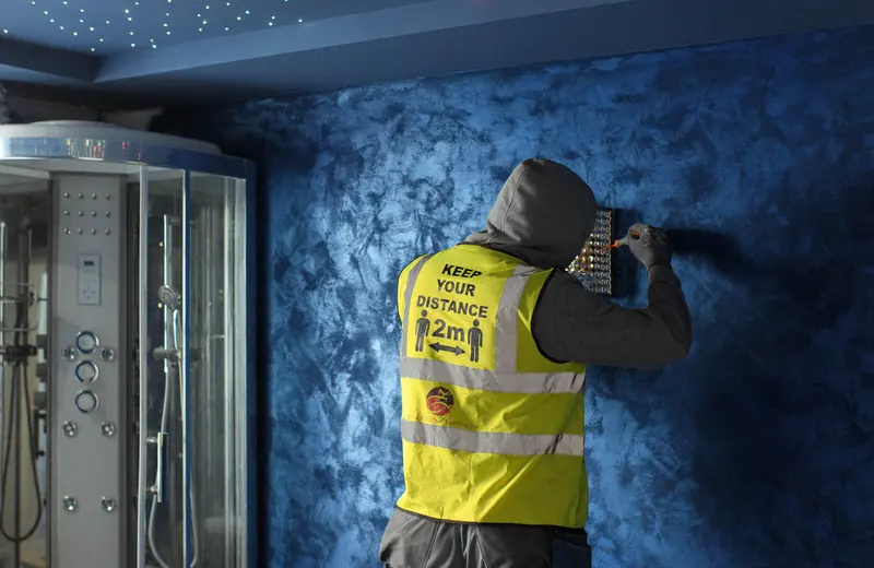 Operative in hi-vis working on a blue textured plaster wall