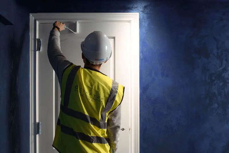 Operative in hi-vis working on a door frame beside a blue plaster wall