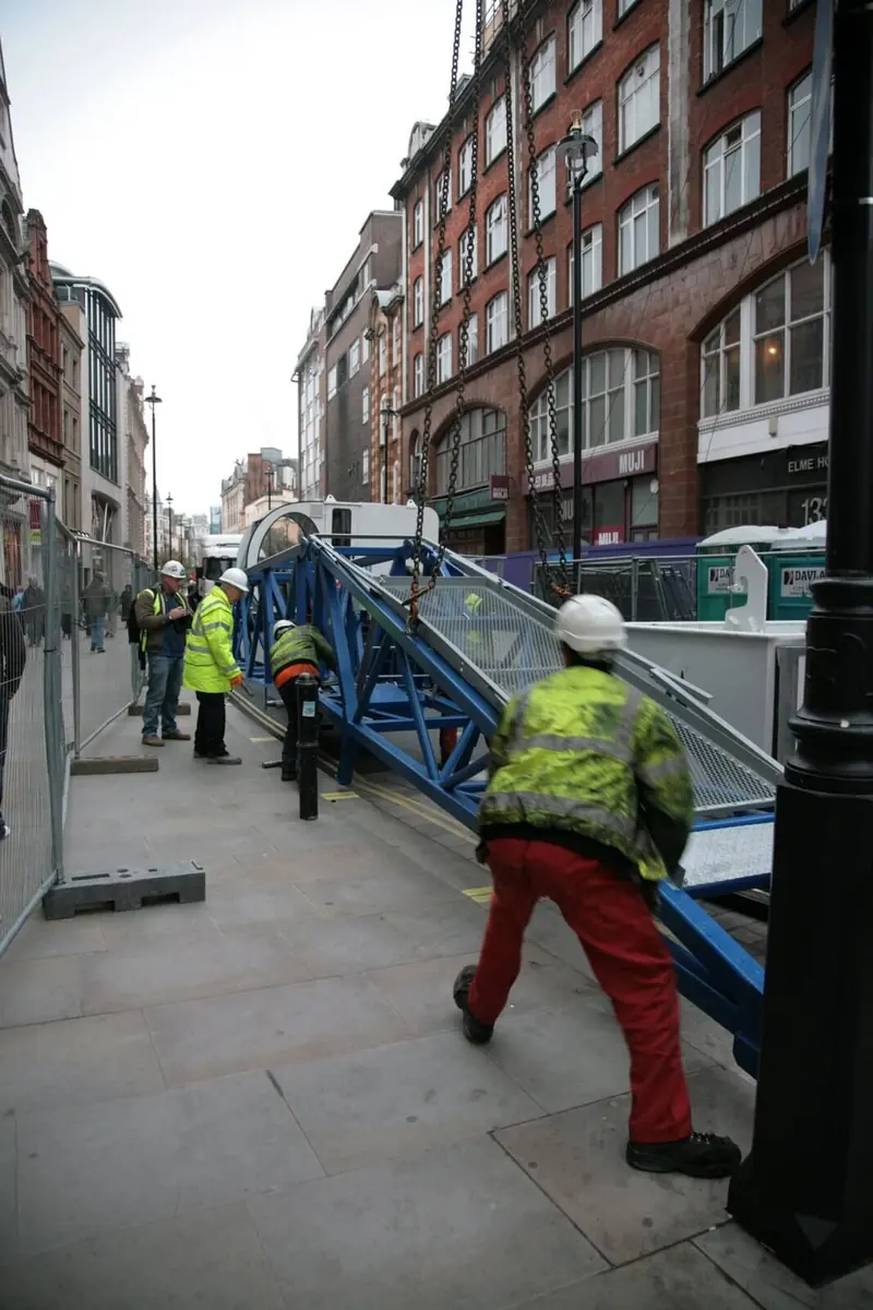 Operative moving a ladder hoist on a London pavement