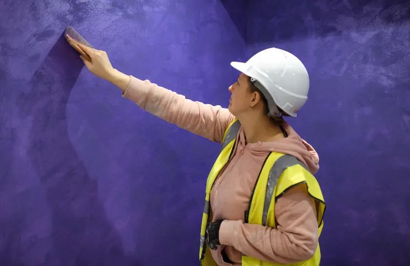 Plasterer in a hard hat applying a finish to a purple wall