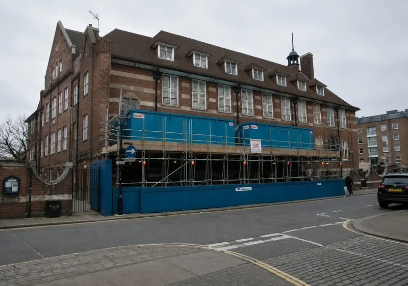Scaffolding and blue hoarding on a red brick school building in London