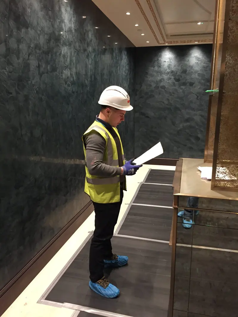 Site manager in a hard hat and hi-vis checking drawings in a corridor with dark polished plaster walls