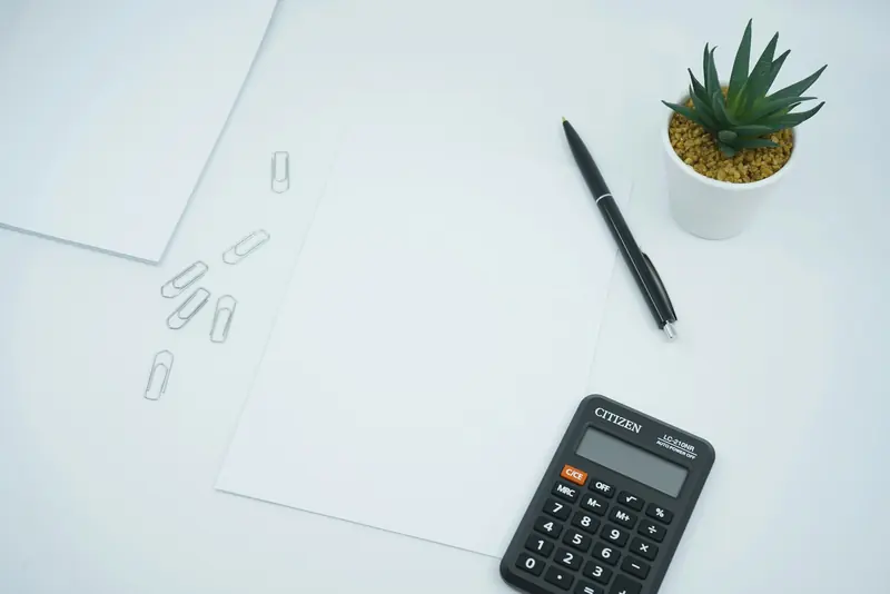 Calculator, pen and blank paper on a white desk