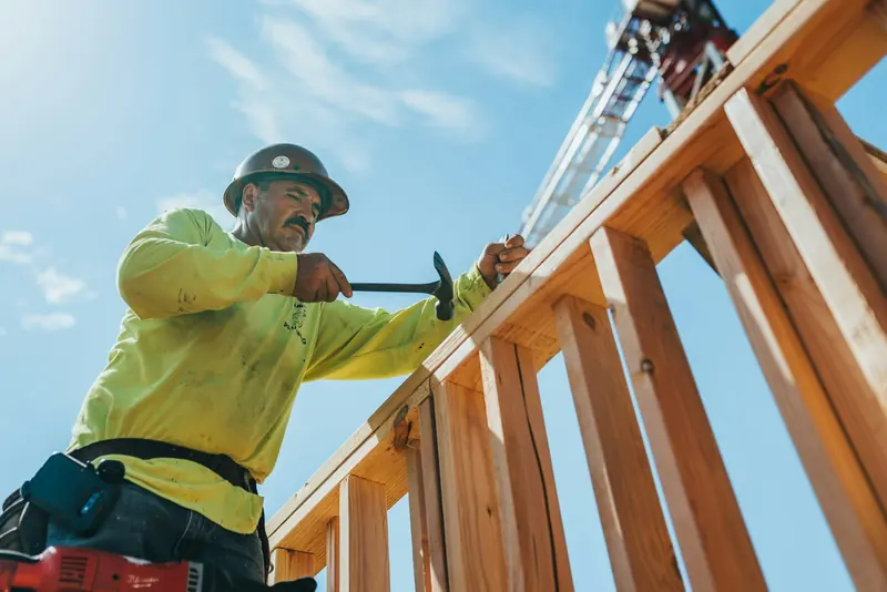 Carpenter in a hard hat nailing a timber frame