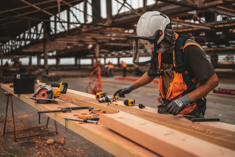 Carpenter in a helmet and hi-vis cutting timber in a workshop