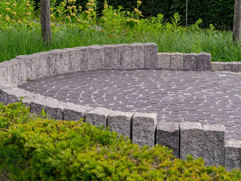 Circular paved patio with a low stone wall and shrubs