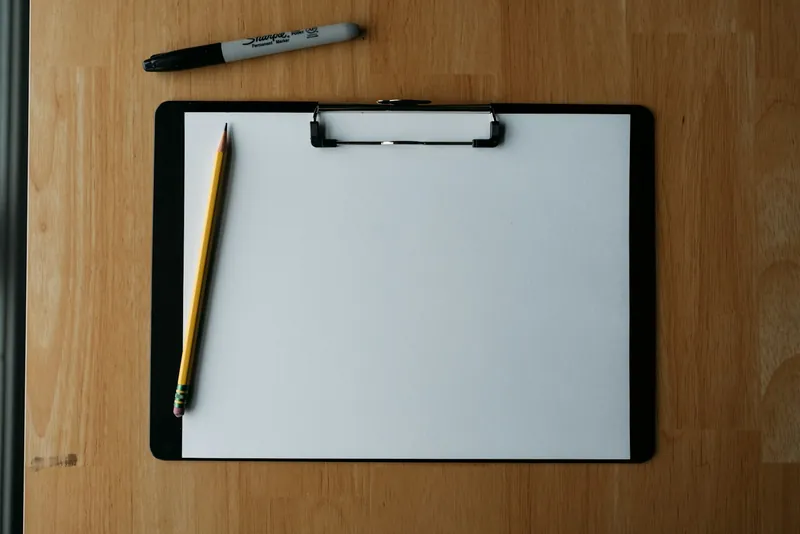 Clipboard with blank paper and a pencil on a wooden desk