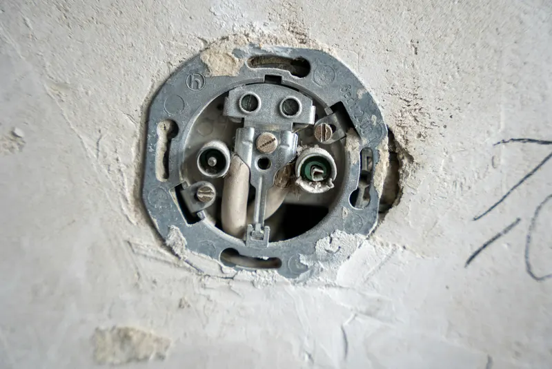 Exposed socket and wiring in a plaster wall