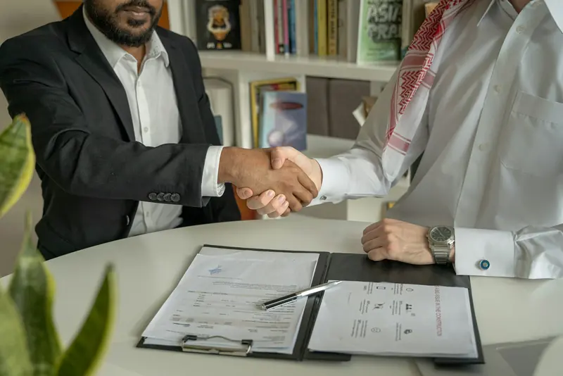 Handshake across a desk over a signed contract