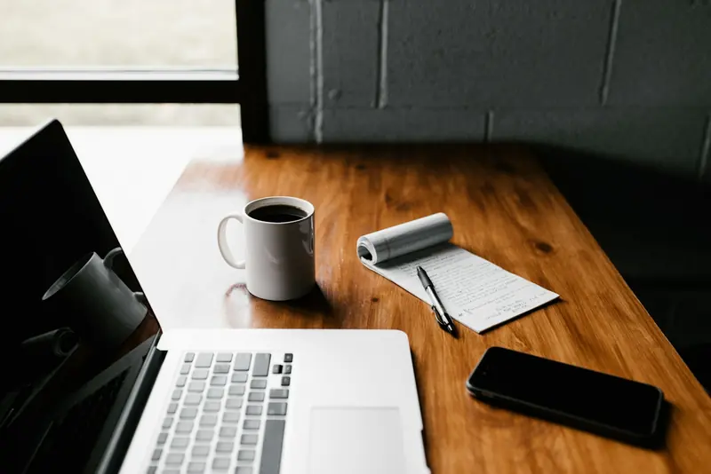 Laptop, coffee mug and notepad on a timber desk