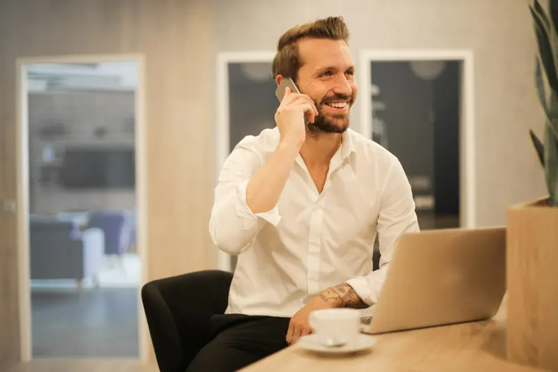 Man on a mobile phone at his desk with a laptop