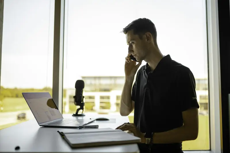 Man taking a call standing by a desk with a laptop