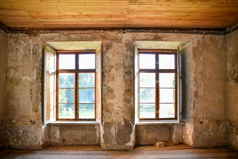 Old room with distressed plaster walls and timber windows awaiting restoration
