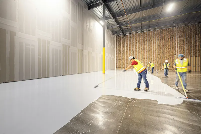 Operatives applying floor coating in an empty warehouse unit