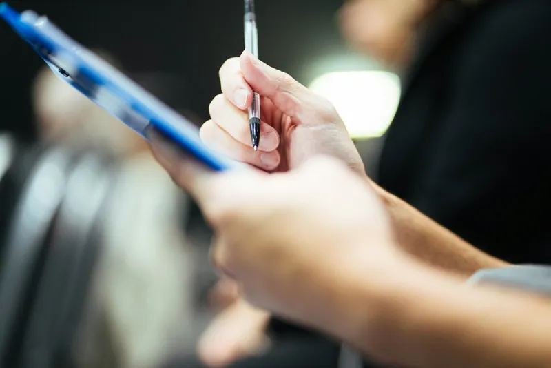 Hand holding a pen over a blue clipboard during an inspection