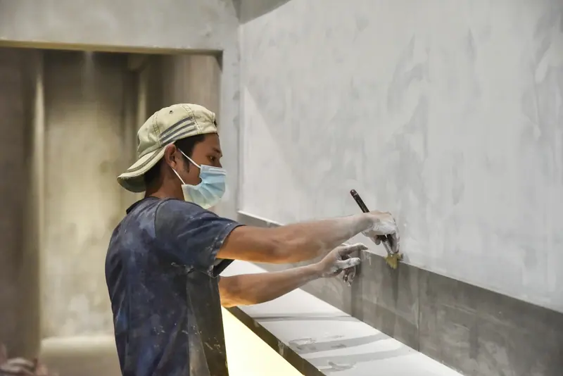 Plasterer in a dust mask skimming a wall with a trowel
