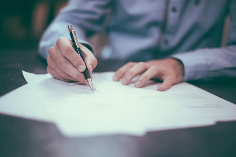 Hand signing a printed contract on a desk