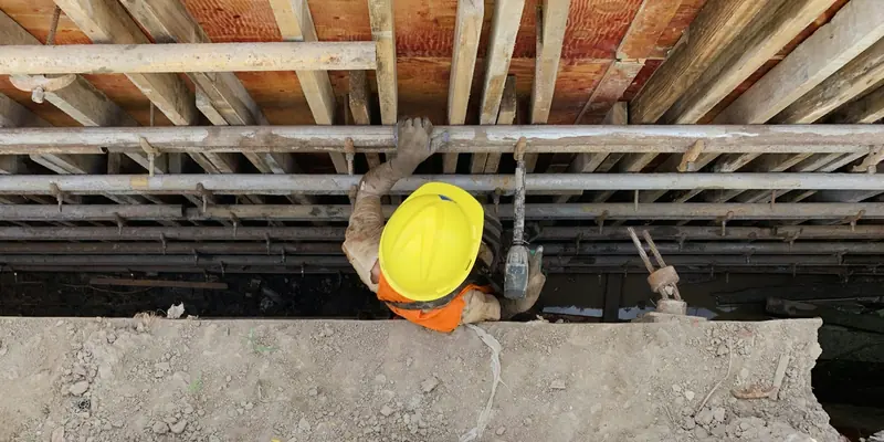 Steel fixer in a yellow hard hat working beneath formwork