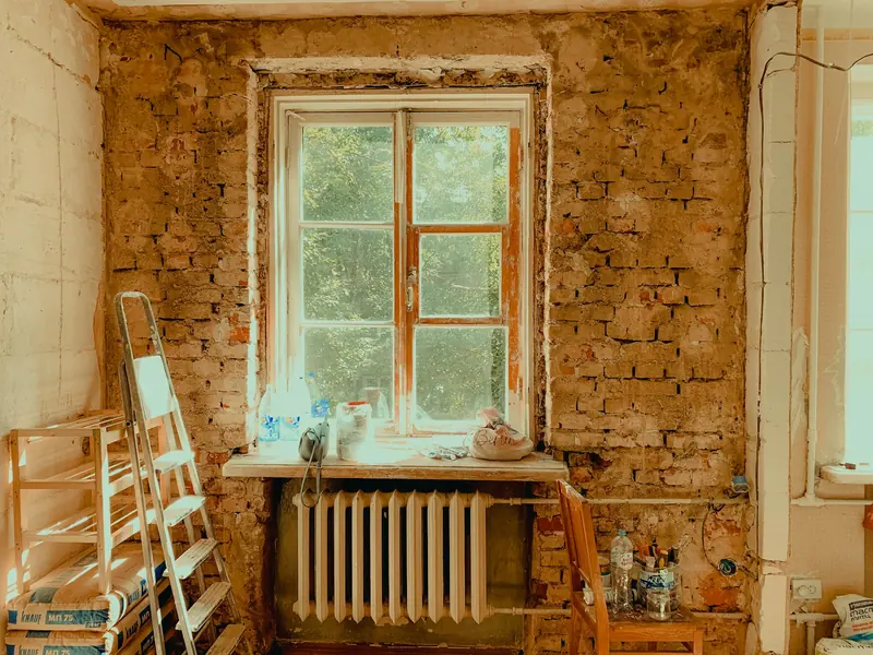 Stripped-back room with exposed brick, radiator and stepladder mid-renovation