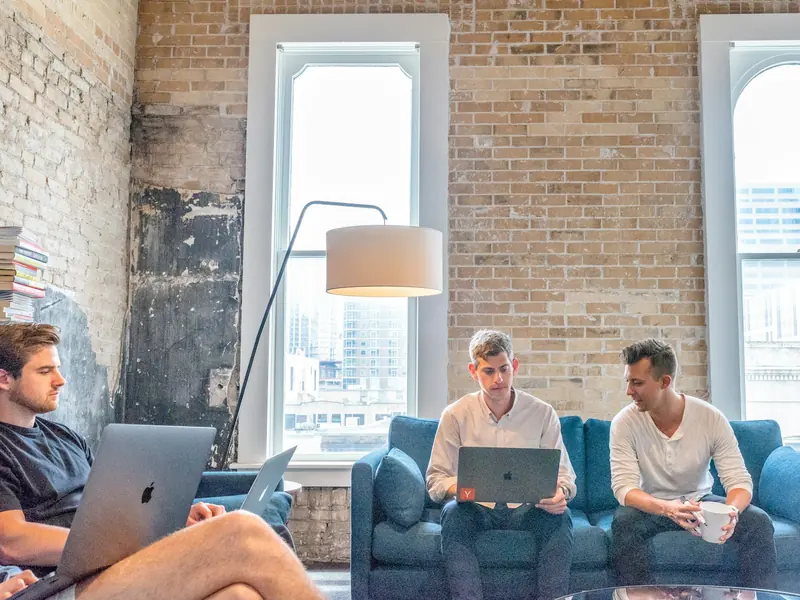 Three men working on laptops in an office lounge