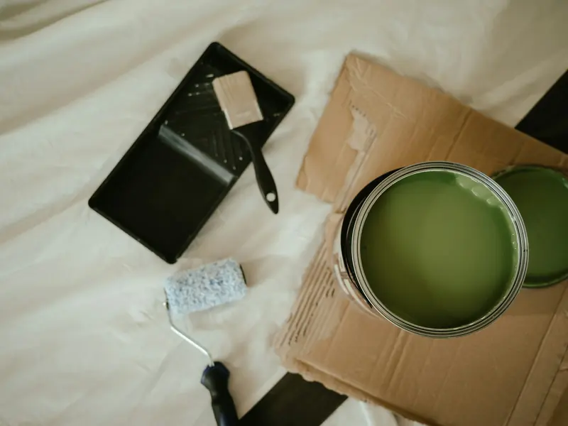 Tin of green paint with a roller and brush on a dust sheet