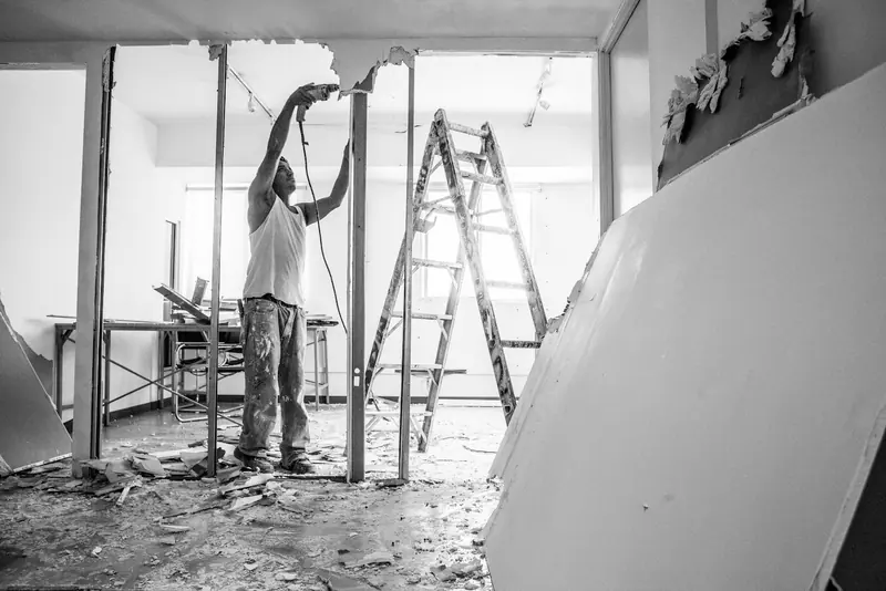 Tradesman fixing plasterboard to metal studs