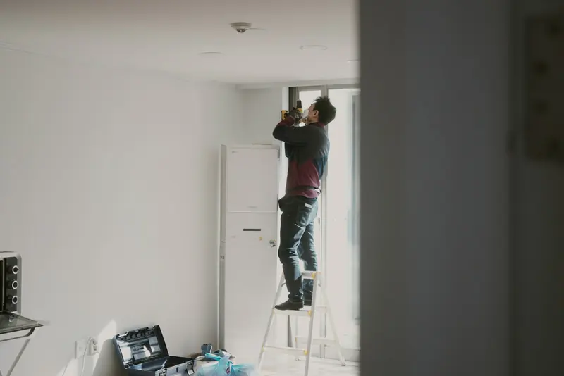Tradesman on a ladder finishing a wall in a newly boarded room