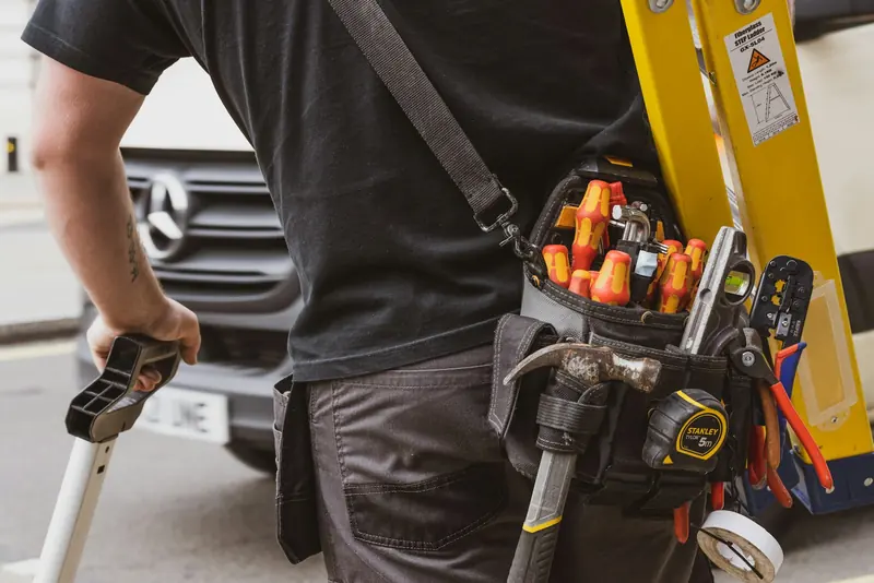 Tradesman with a tool belt and ladder by his van