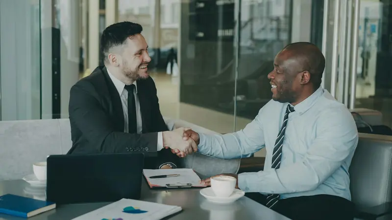Two businessmen shaking hands at a meeting table