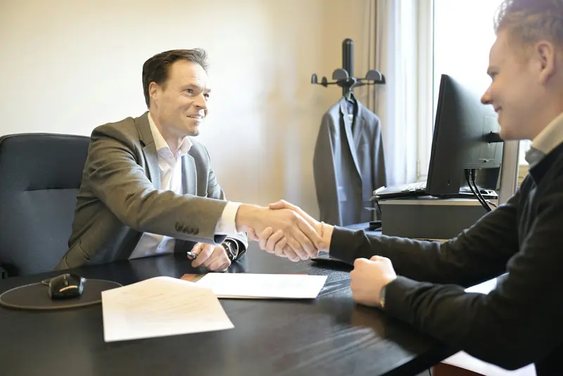 Two men shaking hands across a desk after agreeing a contract