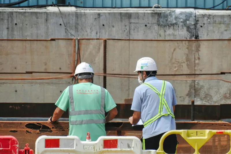 Two operatives in hard hats checking work behind site barriers