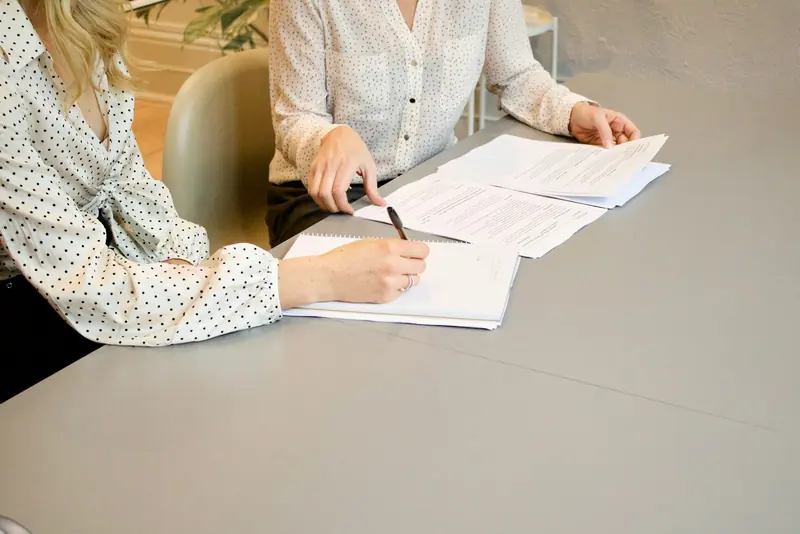 Two people signing documents at a white table