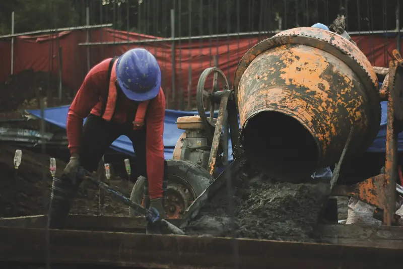 Worker in a hard hat loading a concrete mixer on site