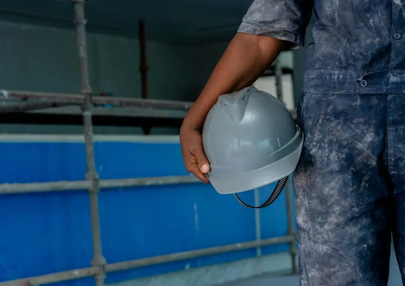 Worker in overalls holding a grey hard hat on site