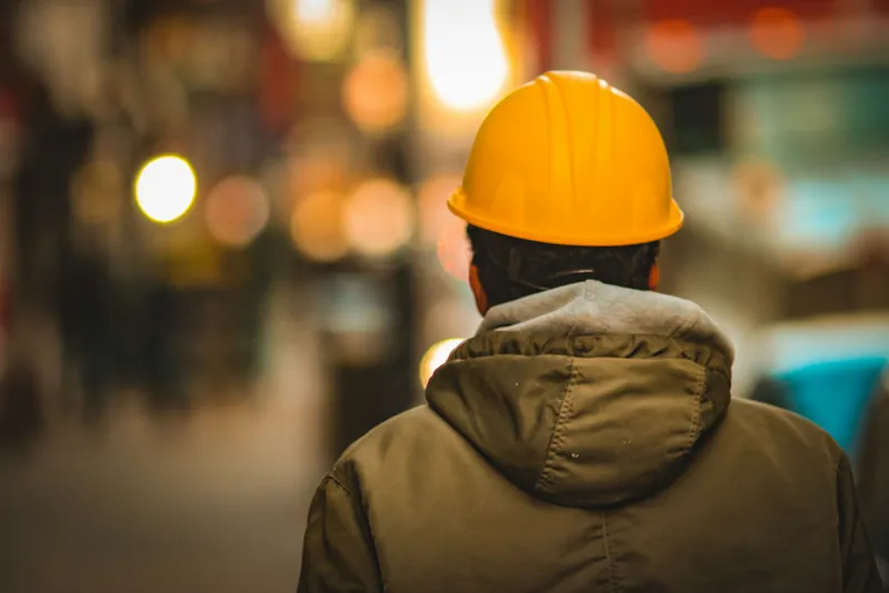 Site worker in a yellow hard hat seen from behind