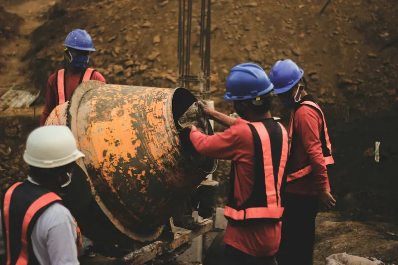 Workers in hard hats feeding a concrete mixer on site