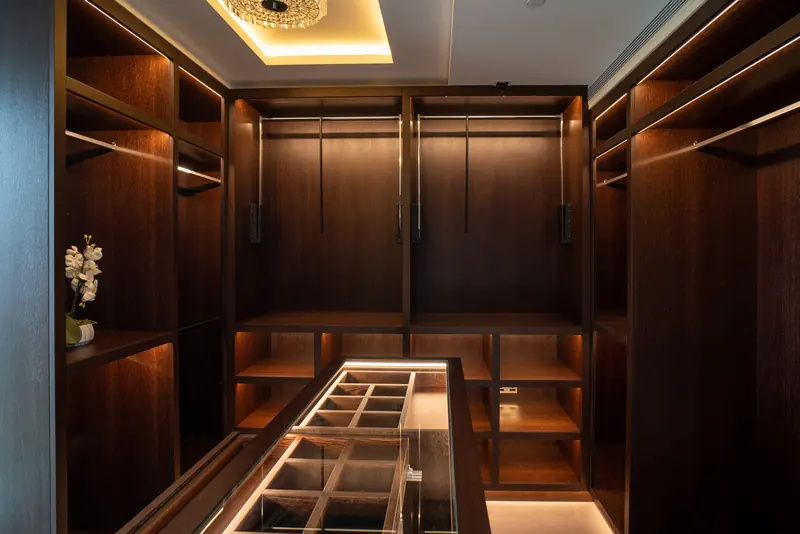Walk-in wardrobe with dark timber joinery and lit shelves